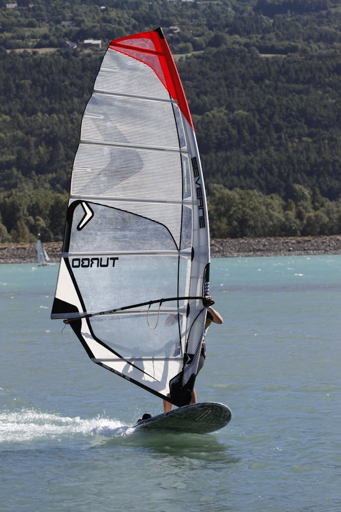A person windsurfing energetically on a serene lake with lush green hills in the background.